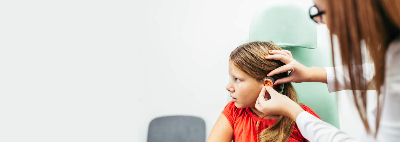 Audiologist fitting hearing aid for a young girl.