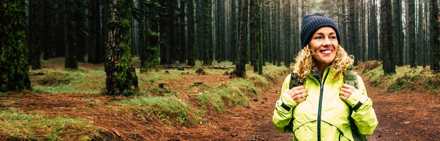 A woman stands in the middle of a forest smiling at the camera