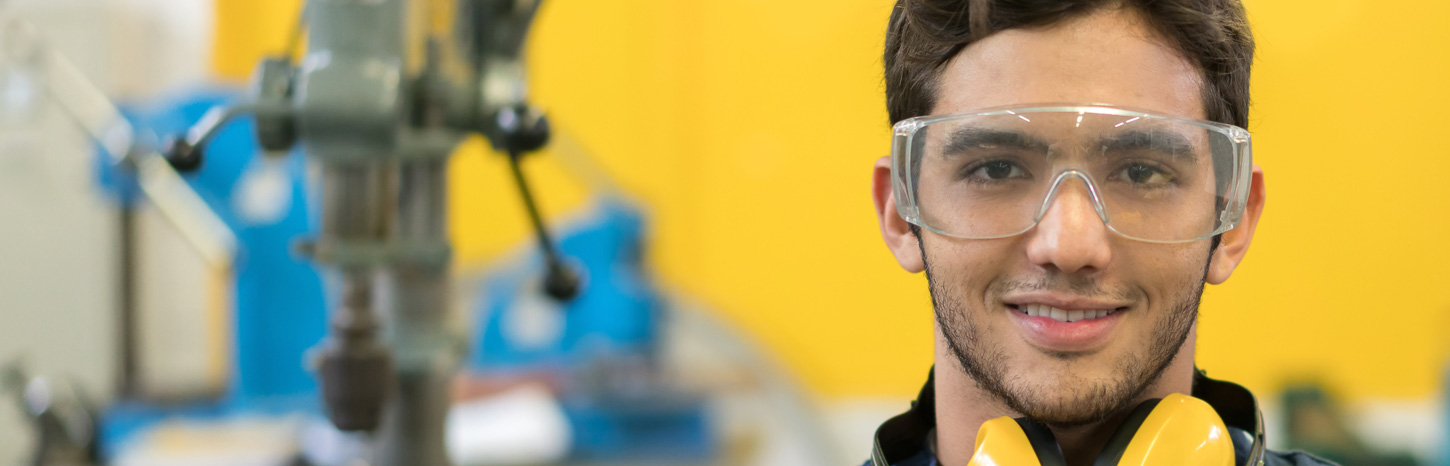 A man with goggles on and ear defenders around his neck smiles at the camera.