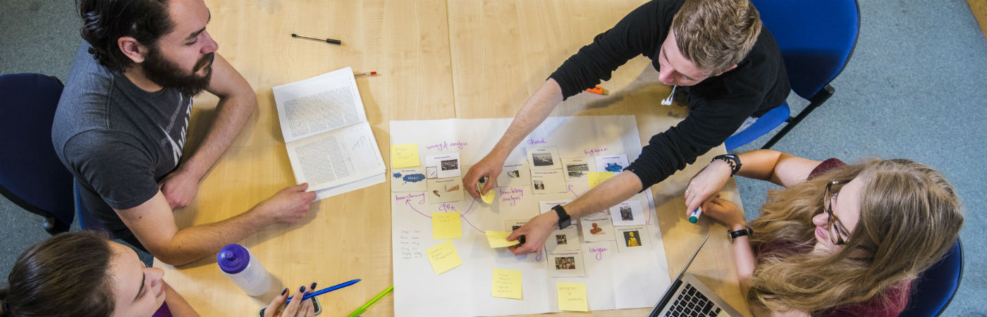 A group of students group around a table sorting post-it notes