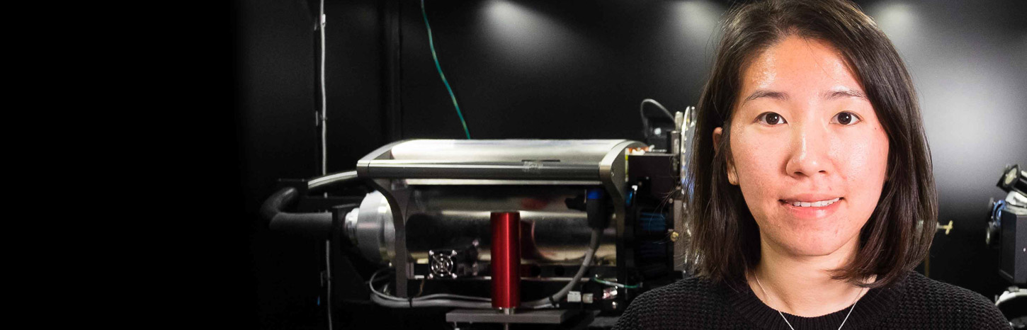 A woman stands in front of scientific equipment in a black room and smiles at the camera.