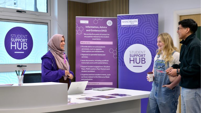 A man and a woman stand in front of a desk smiling while speaking to a member of staff standing behind the desk